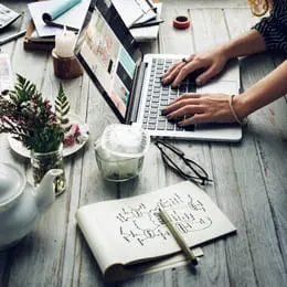 Vu latéral d'un designer WordPress algérien qui conception des sites web sur son PC et utilise à côté du papier